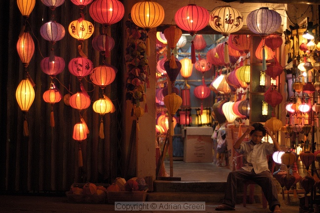 Boy sitting in front of lantern shop during the festival of light in Hoi An