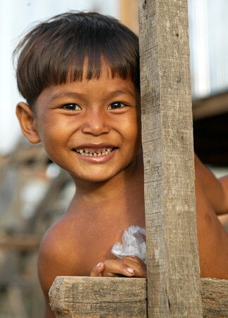Little boy peeping round wooden pole at stileted house, Phnom Penh, Cambodia