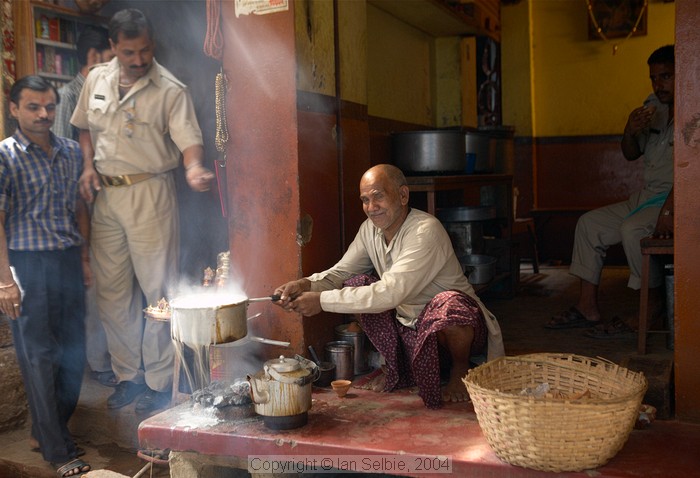 Everyday life in the narrow streets of old Varanasi: the old man has let his milk boil over but seems more amused than upset